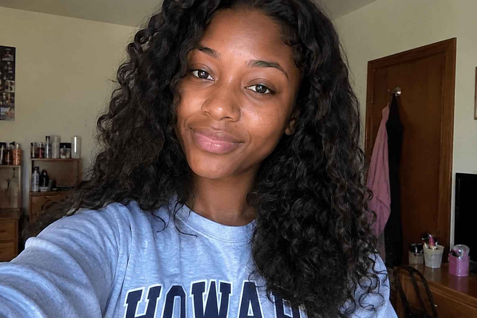 Smiling young Black woman with long, dark curly hair wearing a grey Howard University sweatshirt.